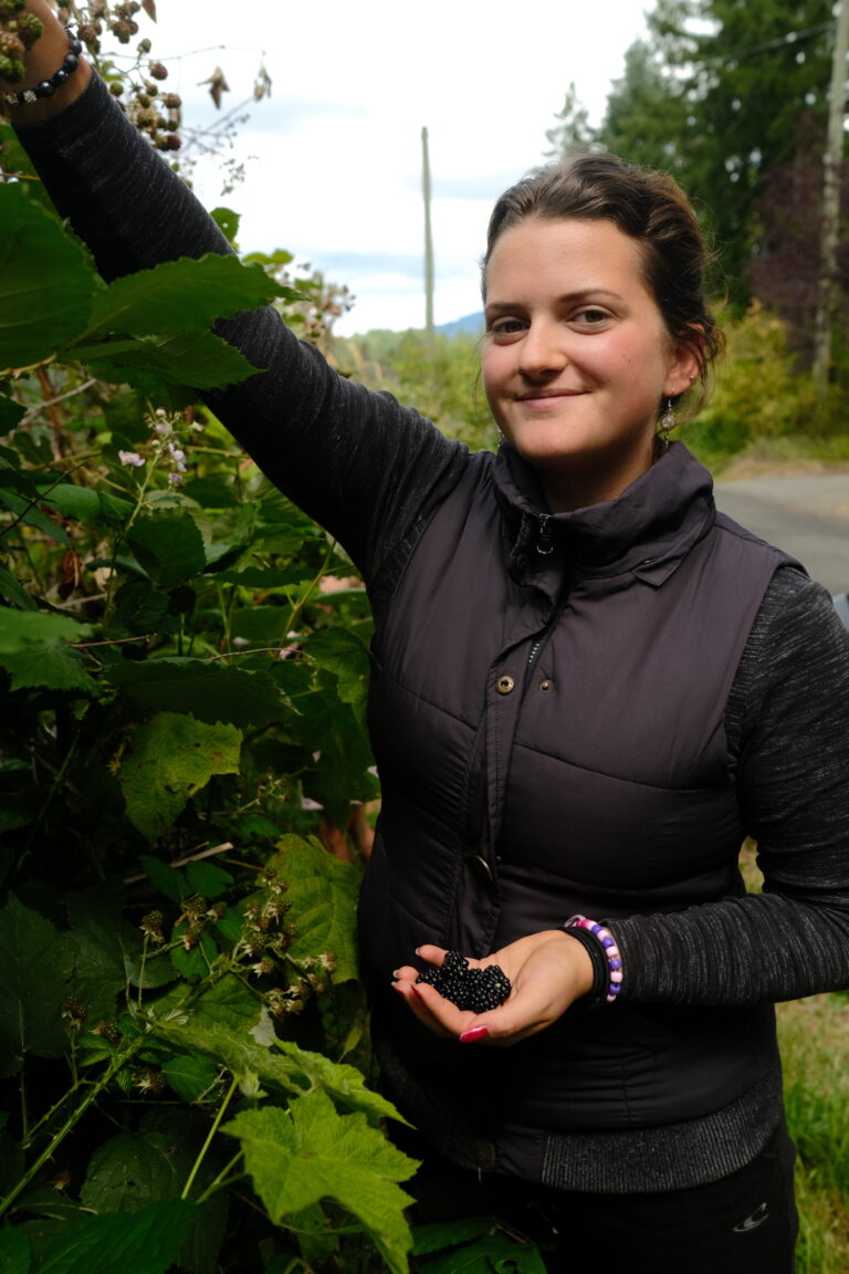 Girl picking blackberries and smiling at camera